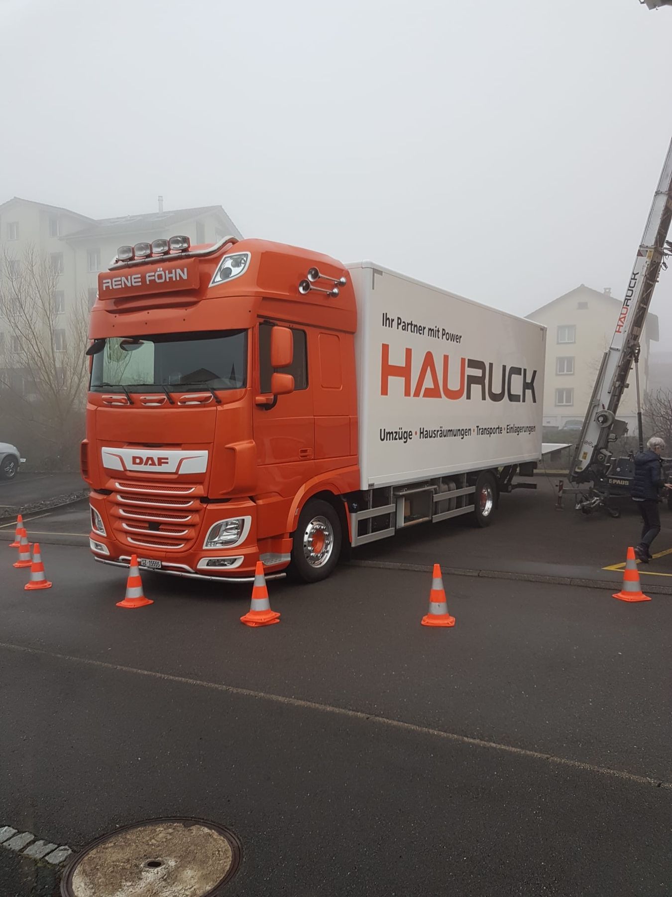 Oranger HAURUCK-Lastwagen auf nasser Strasse mit Pylonen