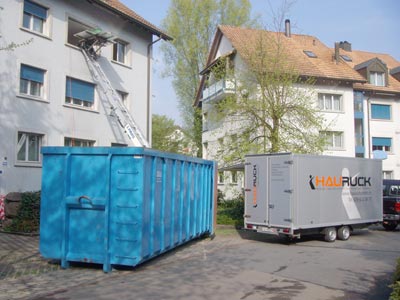 Mulde und HAURUCK-Anhänger vor einem Haus